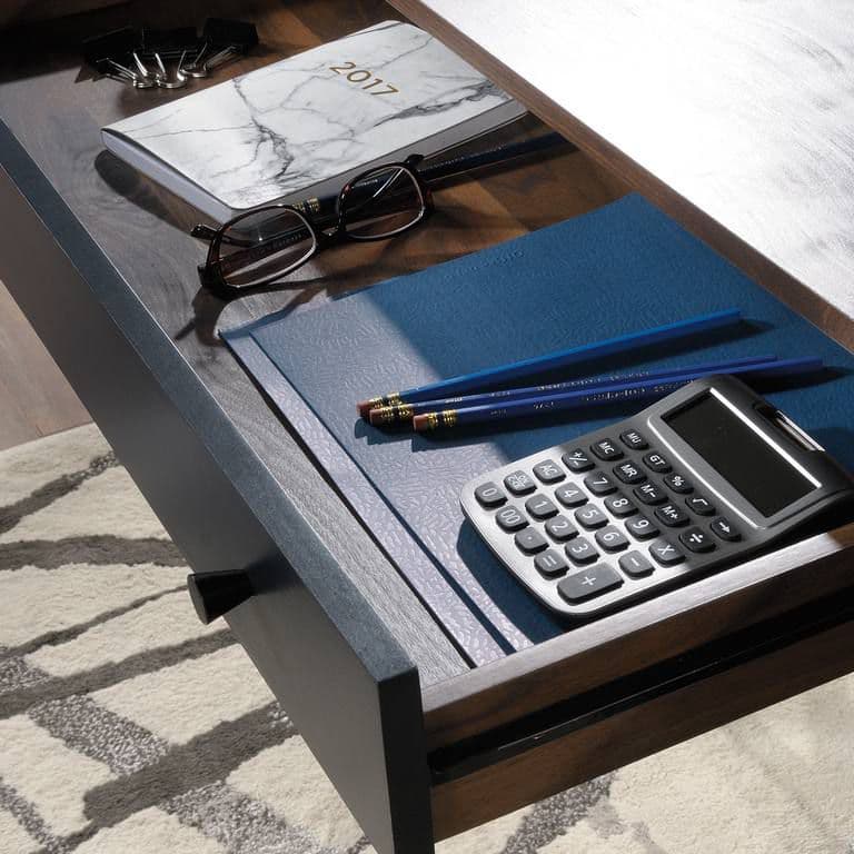 a desk with a calculator, pen, eyeglasses, and notebook